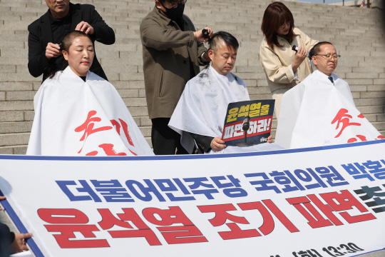 지난 3월11일 국회 본청 앞 계단에서 더불어민주당 전진숙(왼쪽부터)·박홍배·김문수 의원이 윤석열 대통령 조기파면 등을 촉구하며 삭발하고 있다. 여성으로서 삭발에 동참한 전진숙 의원은 "자른 머리카락으로 짚신을 지어 헌법재판소에 보내겠다"며 의지를 드러냈다.<연합뉴스 사진>
